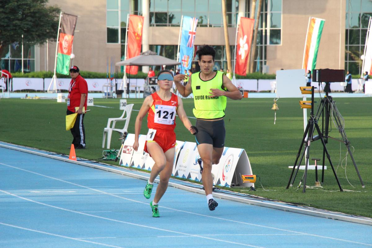 A visually impaired runner runs with her guide