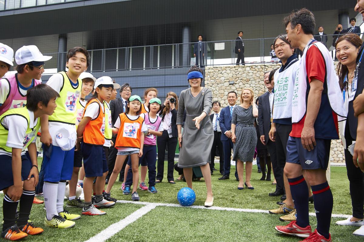 Woman in smart grey dress, blindfolded, surrounded by kids