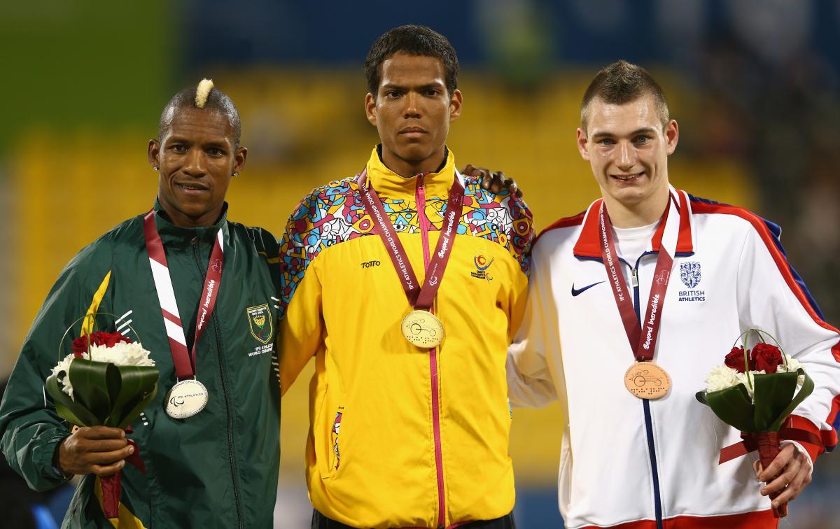 Colombian athlete Dixon Hooker poses on the podium with his gold medal next to the silver and bronze medallists.