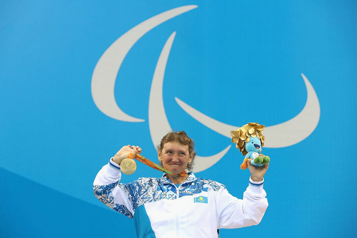 Woman on podium in a wheelchair, showing a medal