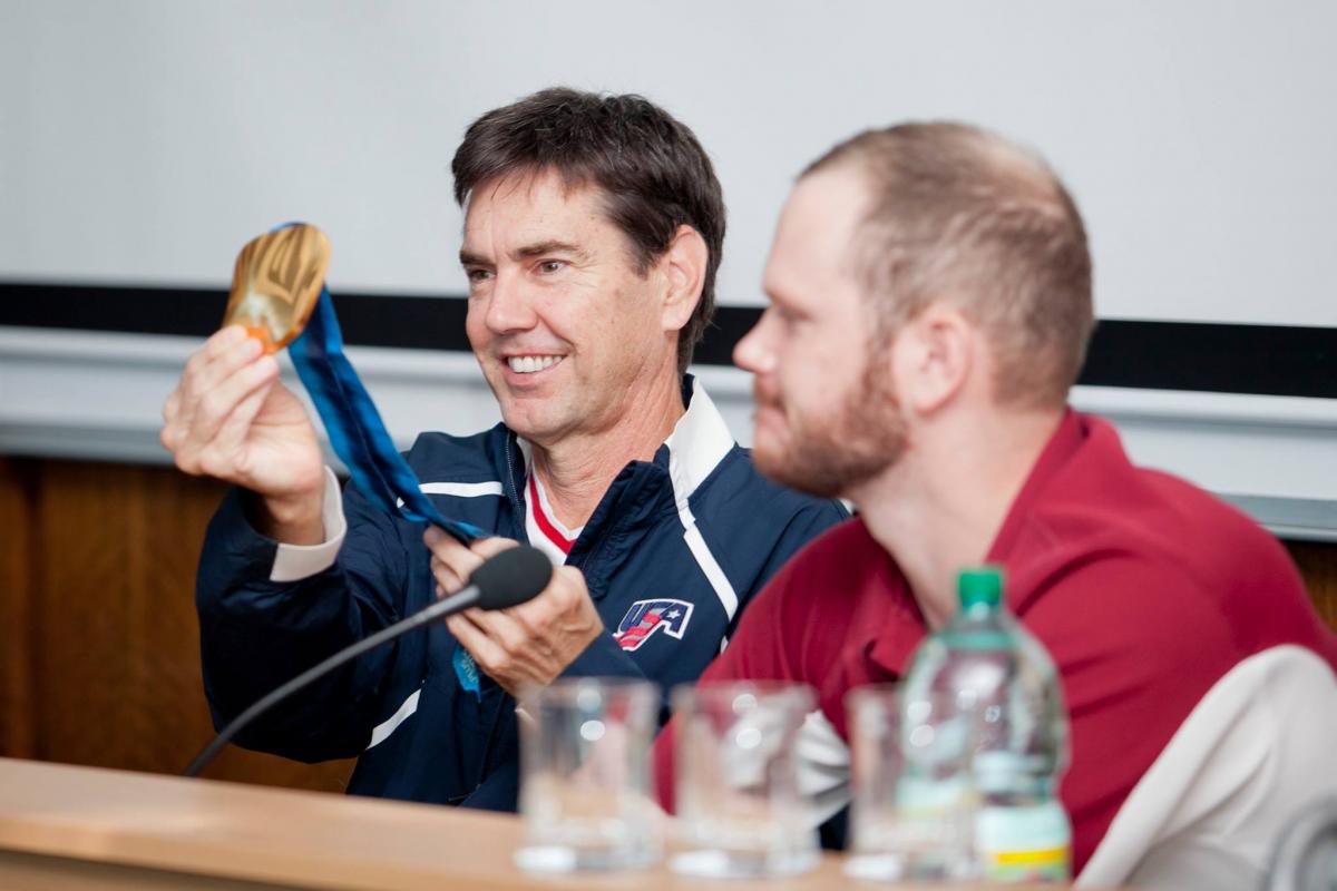 Two men on a podium, one showing a medal