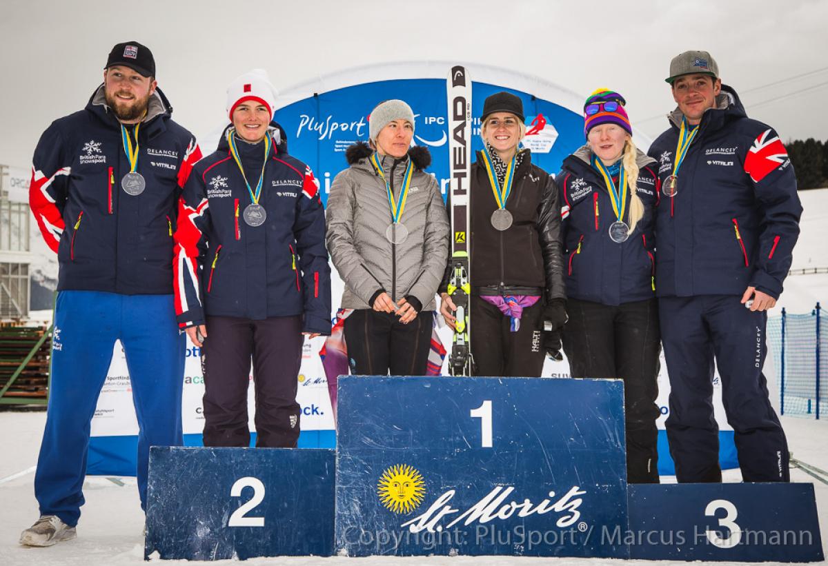 Three female alpine skiers and their guides standing on the podium