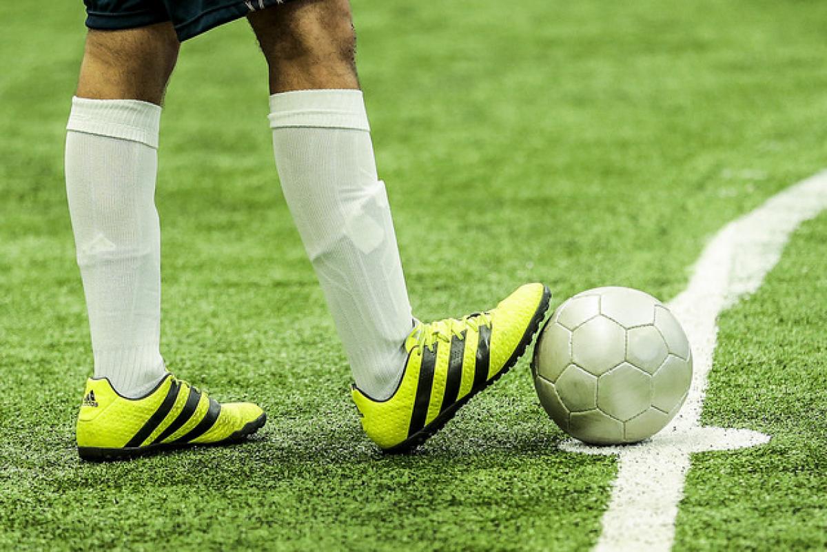 Football at SP2017 A man withbright yellow football boots rests his foot on a ball.