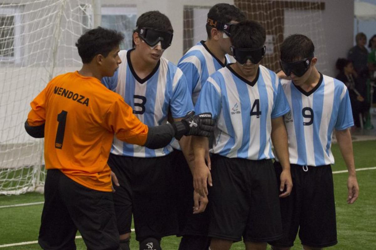 A blind football team organise themselves on the pitch