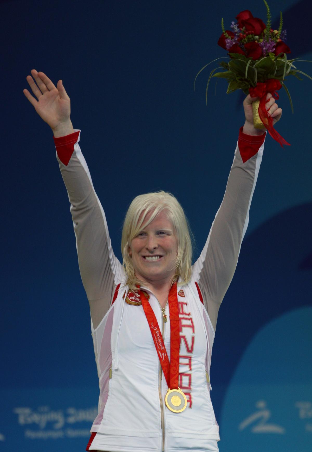 Swimmer raises her arms on the podium to celebrate her medal