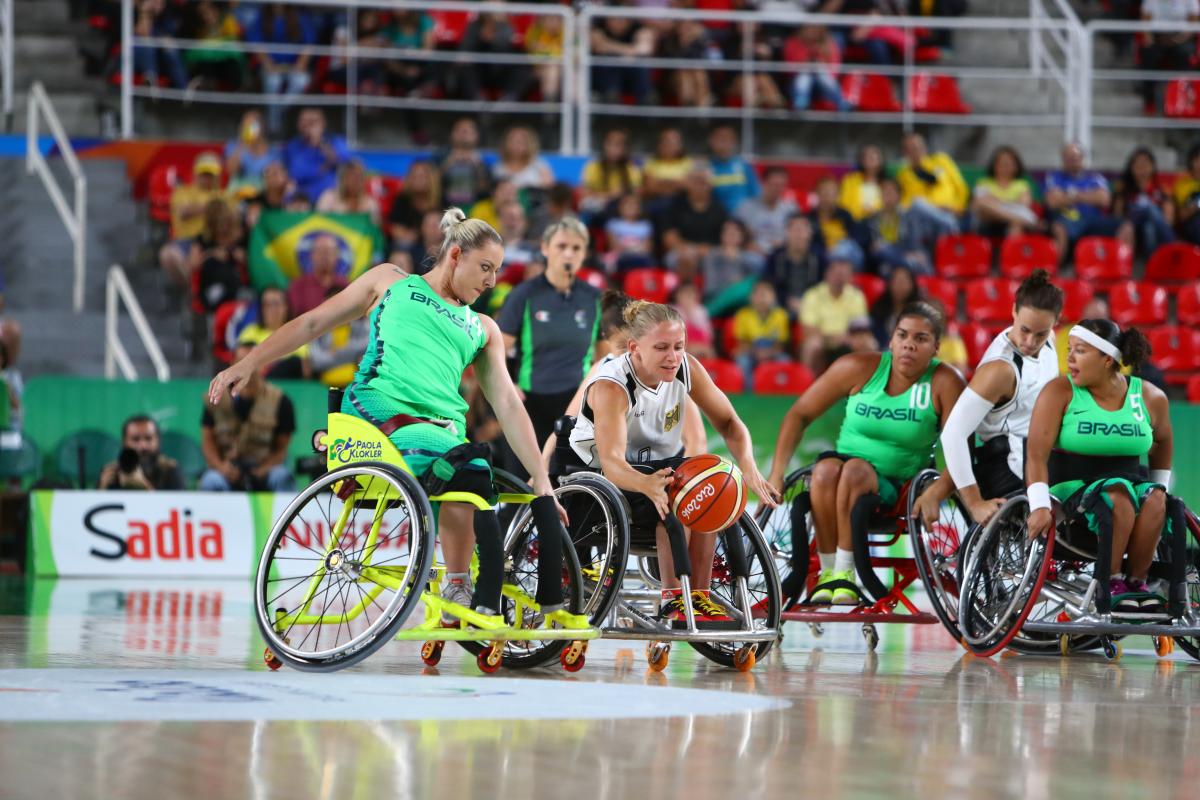 Woman in wheelchair goes for loose basketball while oppents guard her