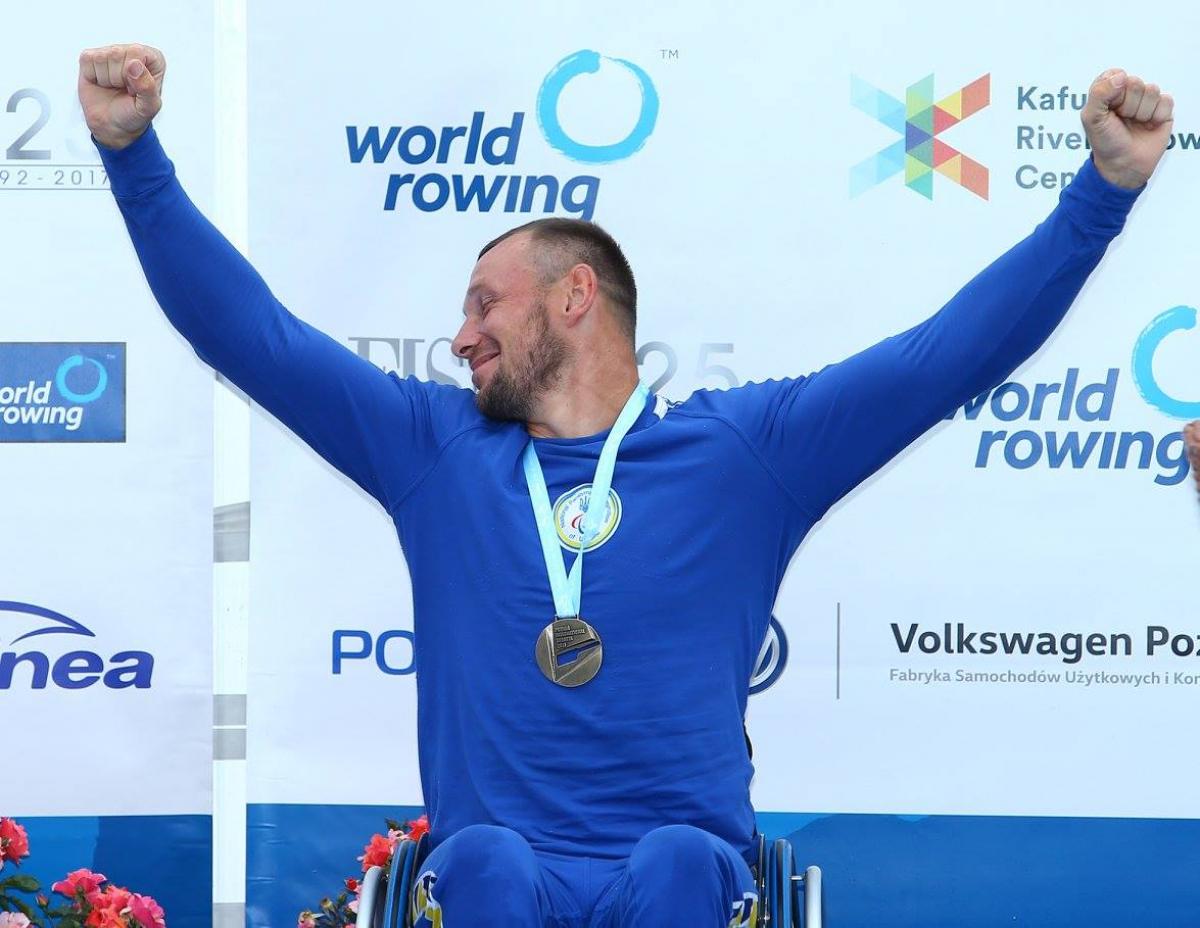 rower raises arms to celebrate gold medal on podium