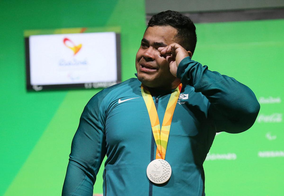 man cries while holding silver medal on podium