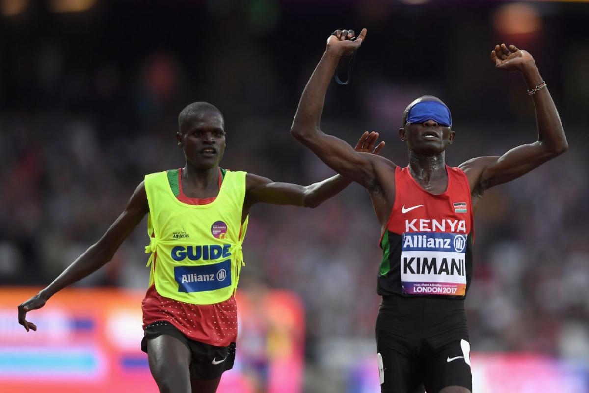 a blindfolded runner and his guide celebrate after crossing the finish line 