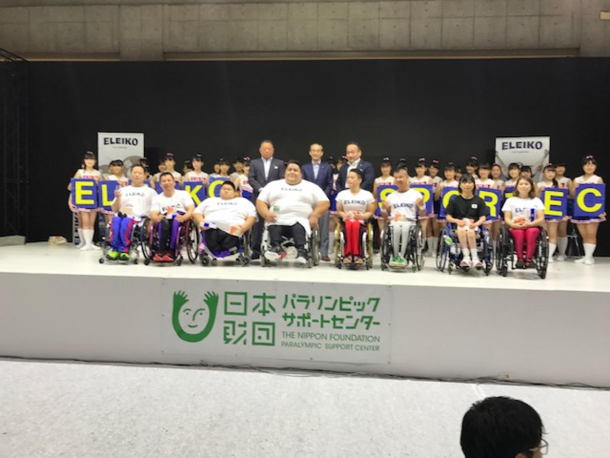 a Para powerlifter on a stage surrounded by young children