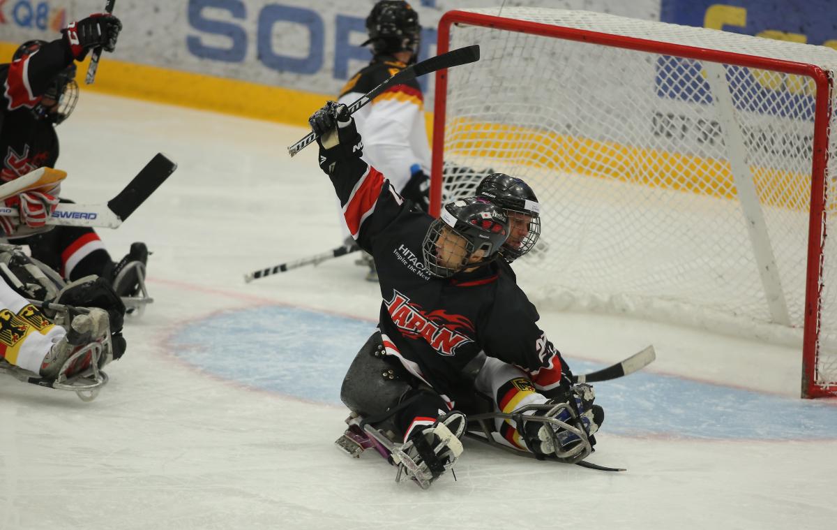 a Para ice hockey player raises his arm in celebration at a goal