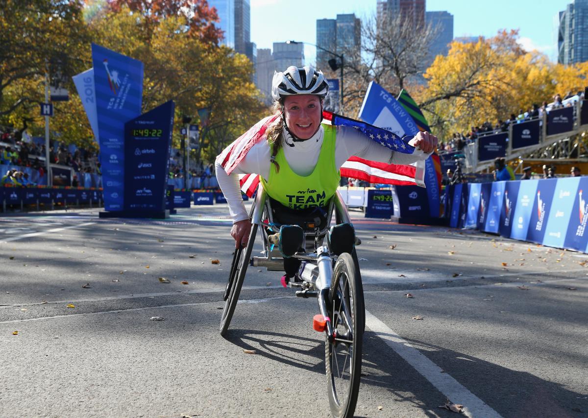 a female Para wheelchair racer celebrates with an American flag