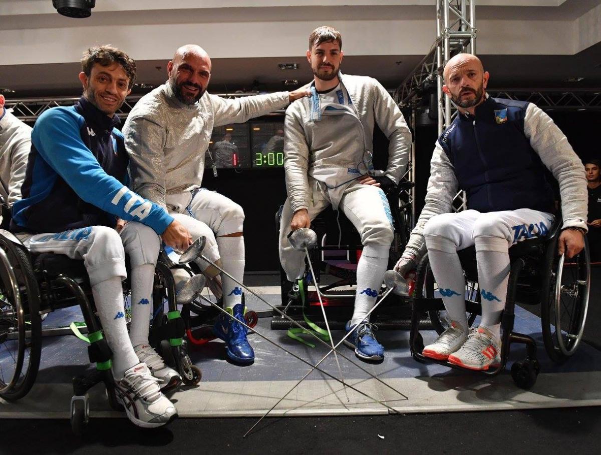 Four male wheelchair fencers pose with their swords 