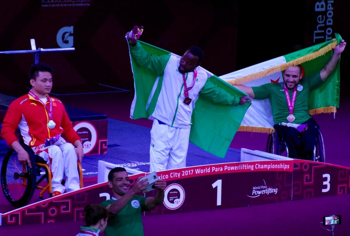 three powerlifters on the podium, two holding up flags