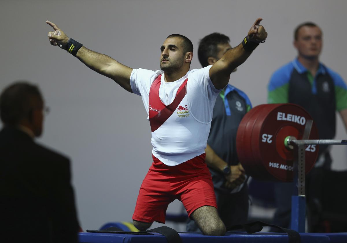 a male powerlifter raises his arms in celebration on the bench