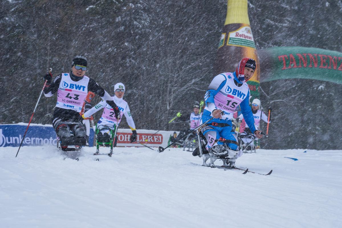 a group of male sit skiers race on the snow