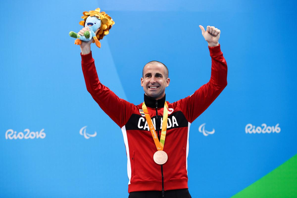 a male Para swimmer raises his arms on the podium