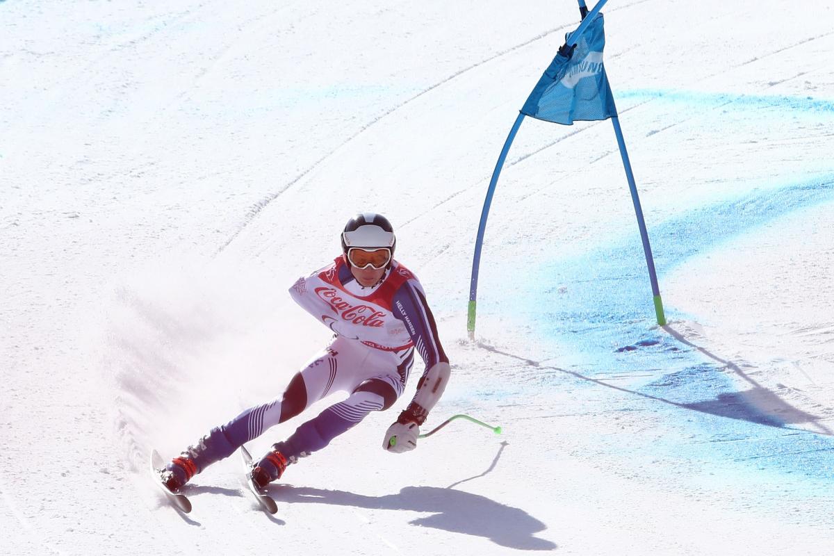 a male Para alpine skier rounds a gate