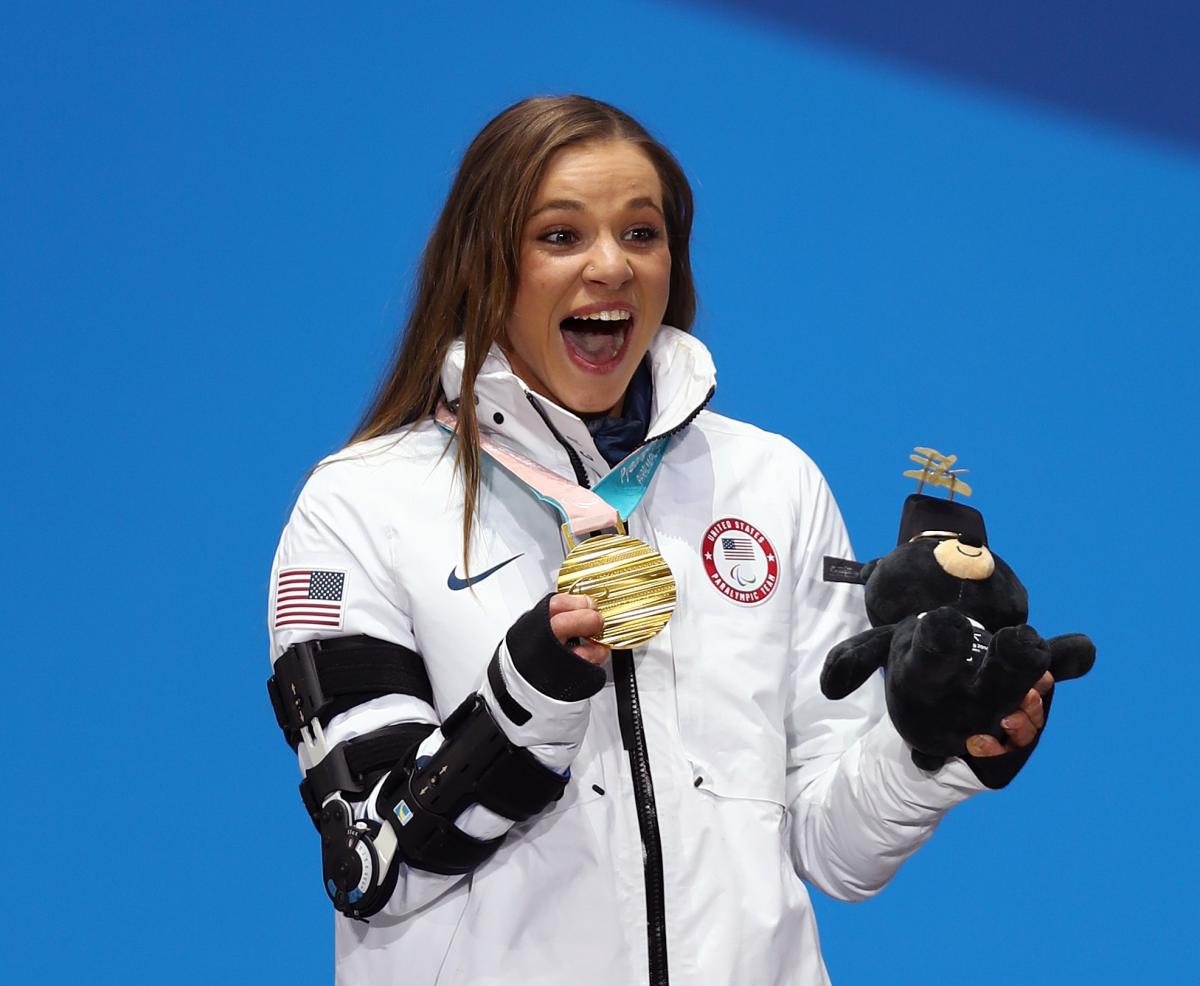 a female Para athlete holds up her gold medal and her mascot