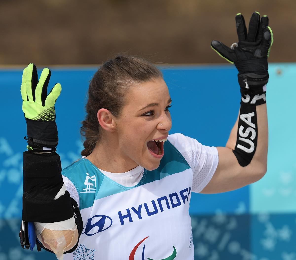 a female sit skier throws up her arms in celebration