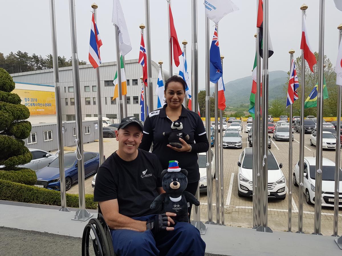 a male Para athlete and a woman standing both holding mascots