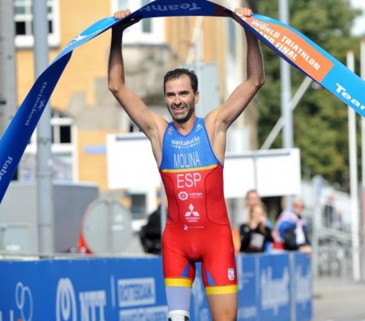 a male Para triathlete holds up the finish line tape as he crosses