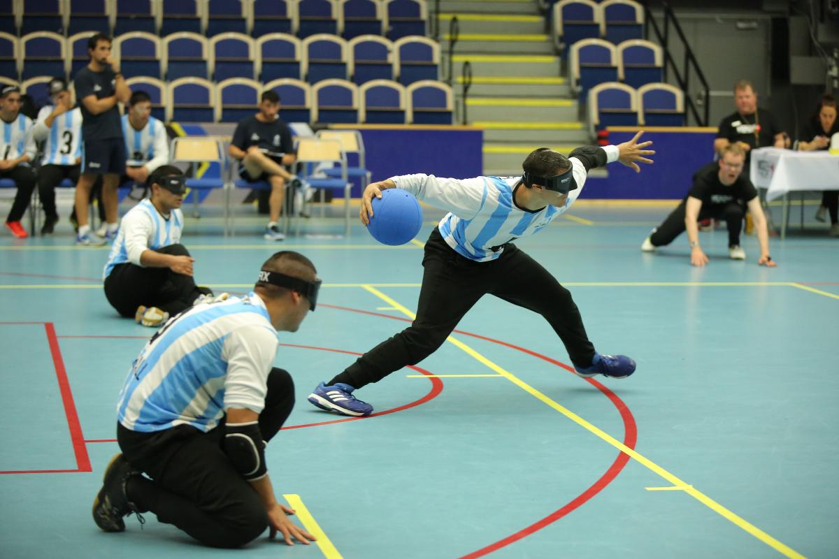 a male goalball player prepares to take a shot while two others wait beside him