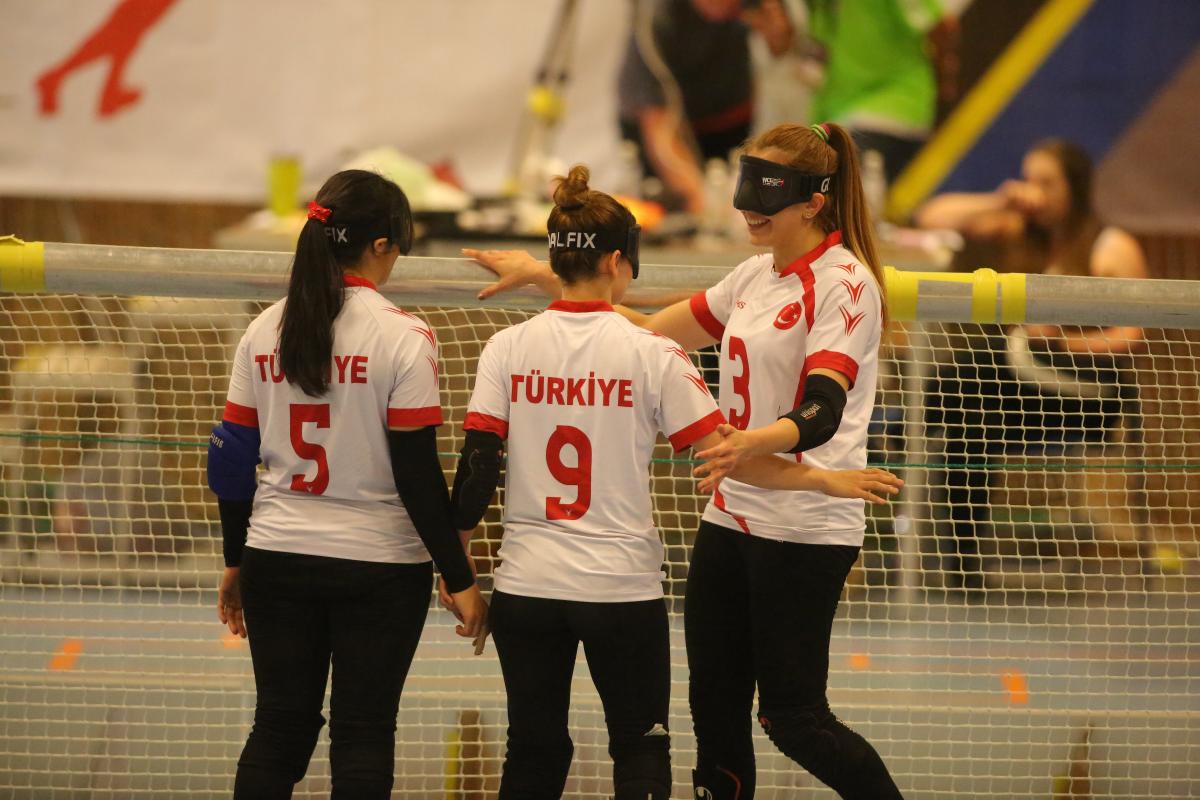 three female goalball players hug in celebration in front of the goal