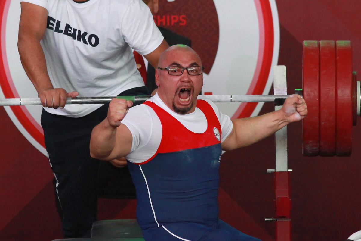 a male powerlifter raises his fists in celebration on the bench