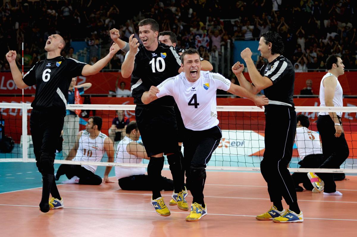 a group of male sitting volleyballers celebrate on the court