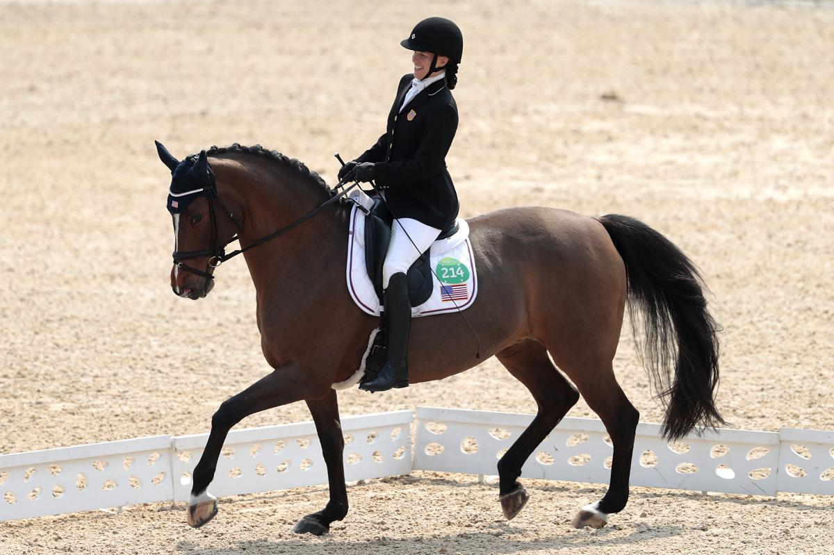 female Para equestrian rider Rebecca Hart competes on a horse in a dressage arena