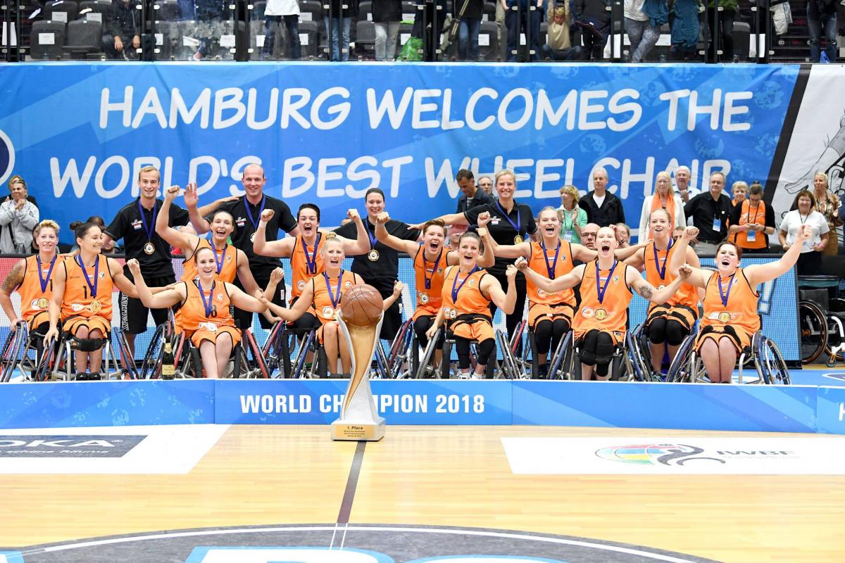 A group of women in organge vests celebrate with a large trophy after winning the world title