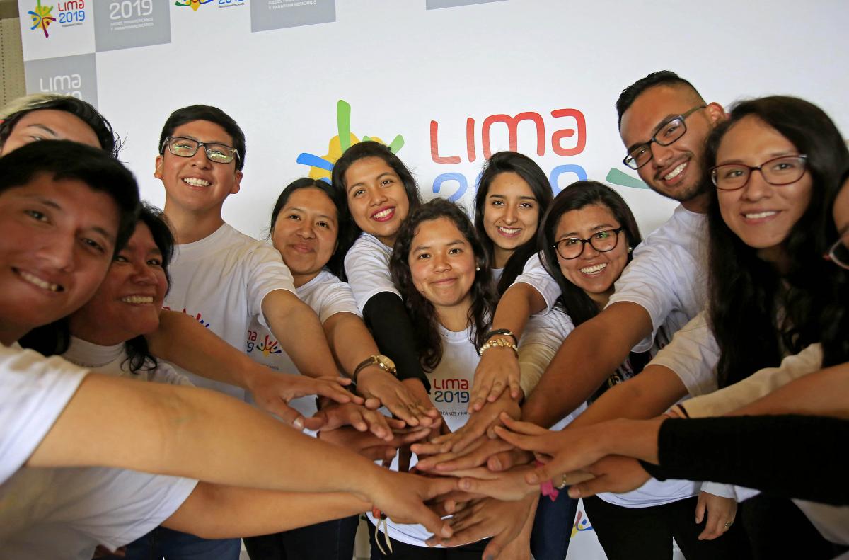 Twelve people smiling and placing their hands on each others'