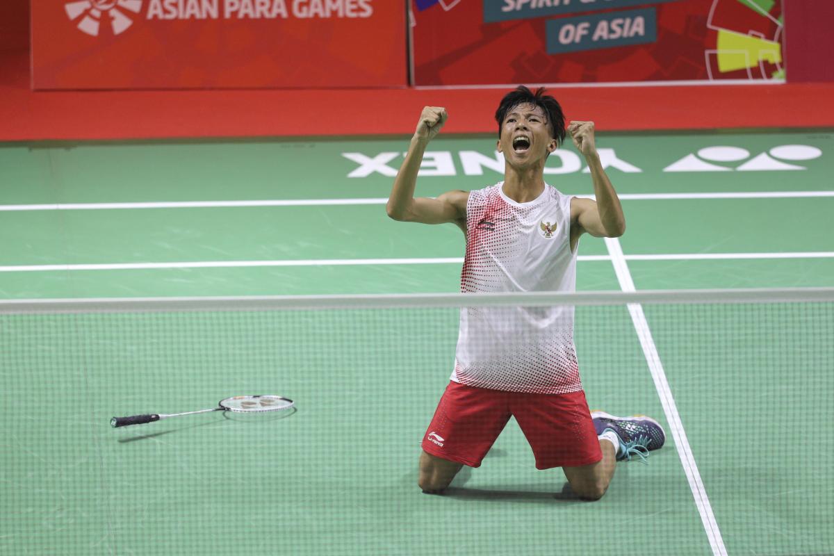 male Para badminton player Dheva Anrimusthi falls to his knees and clenches his fists on the court