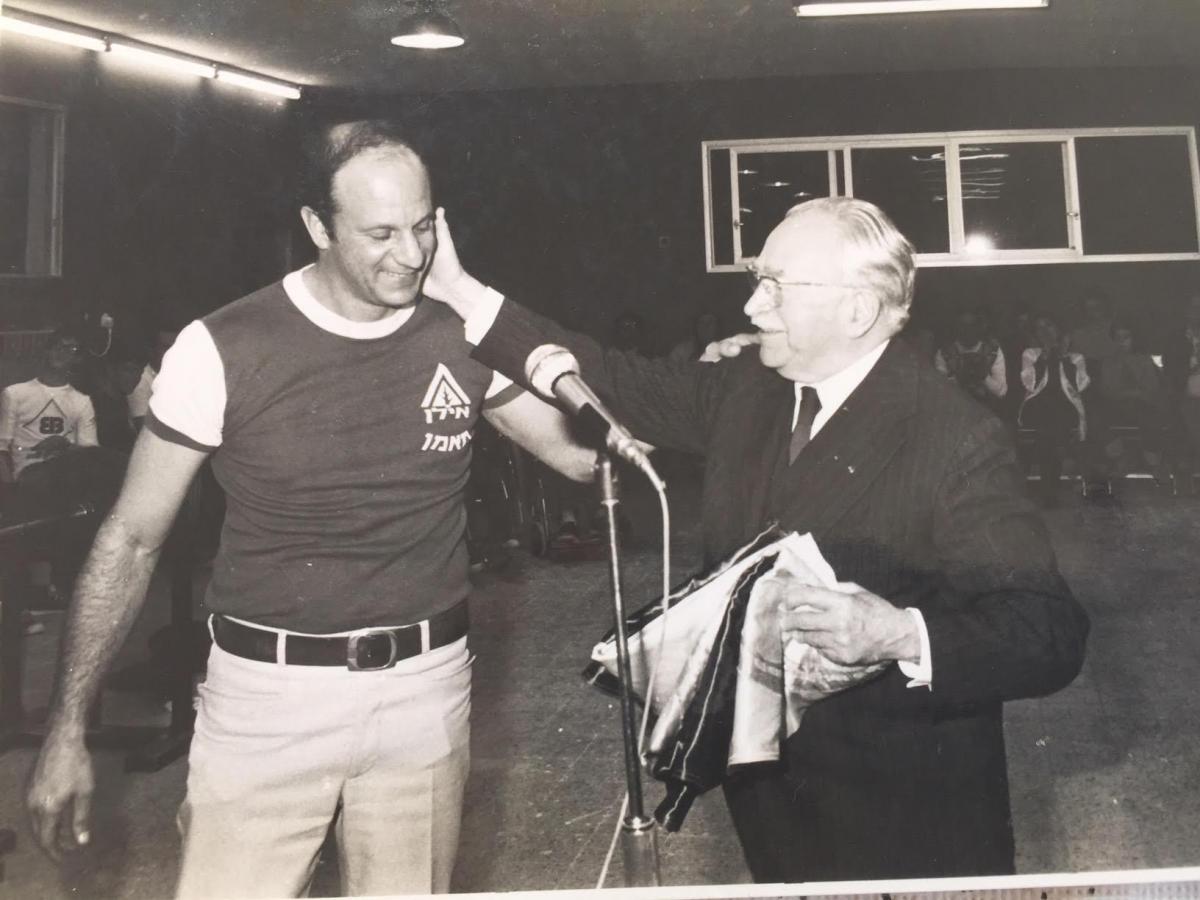 Reuven Heller puts his arm on the shoulder of Sir Ludwig Guttman who is touching his face