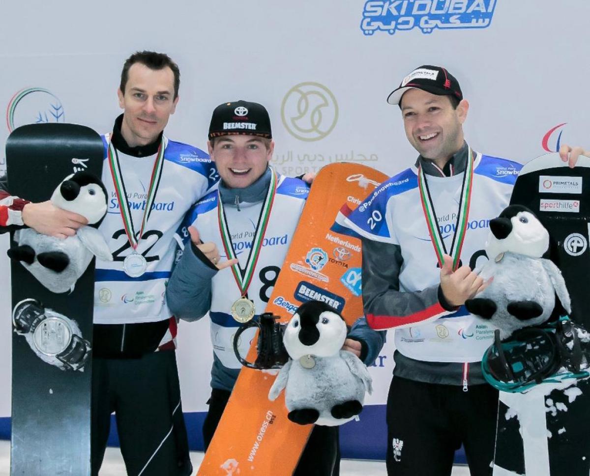 Three men with helmets in an indoor snowboard track