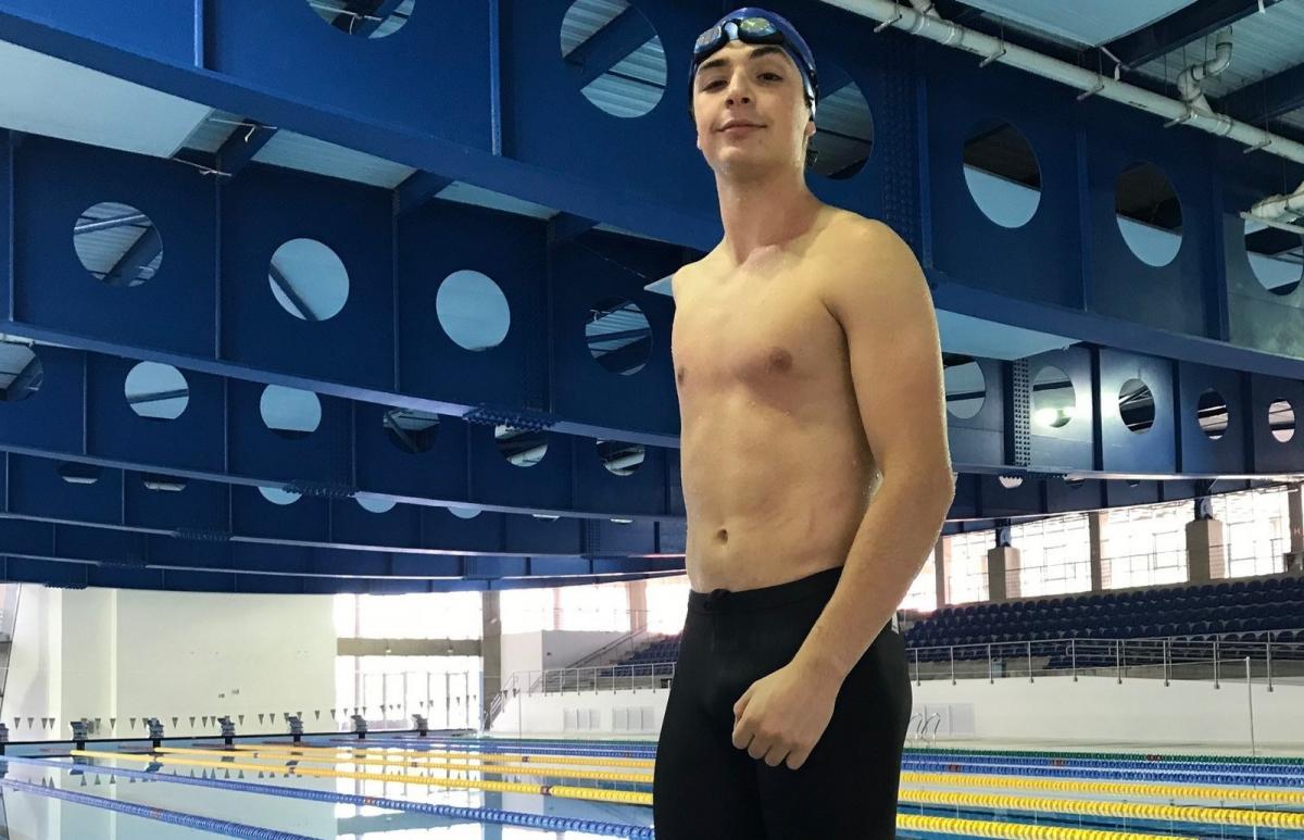 A young athlete withou one arm standing in front of a swimming pool