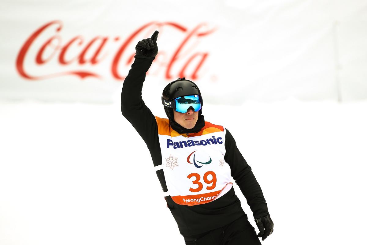 male Para snowboarder Matti Suur-Hamari raises his finger as he crosses the finish line