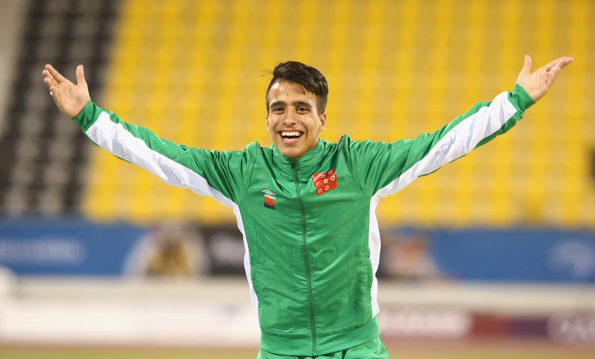 male Para athlete Abdellatif Baka raises his arms in celebration on the podium 