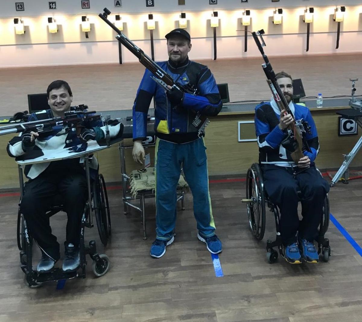 Three male medallists pose with their rifles 