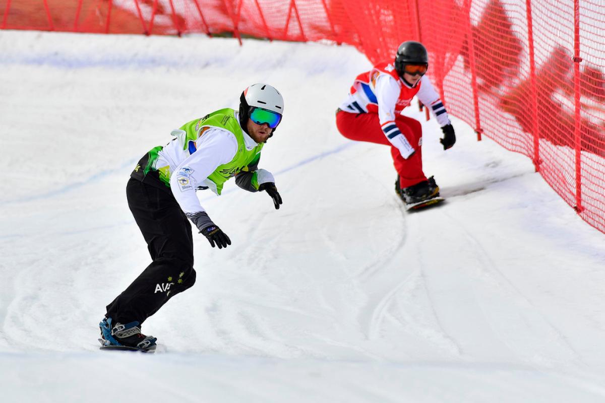 two male Para snowboarders racing down the slope head to head 