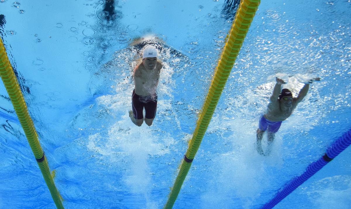 An armless man swimming next to a short stature man