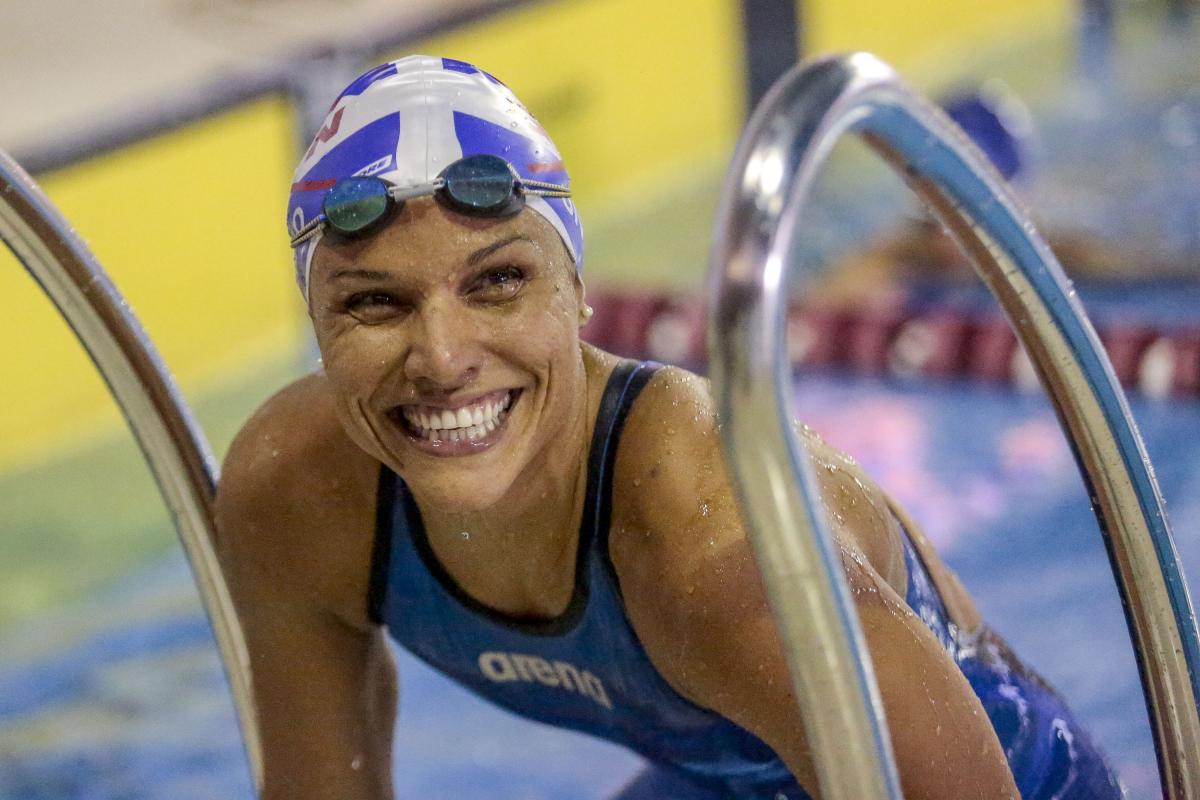 Female Para swimmer Maria Carolina Gomes smiles in the pool while leaning on the steps