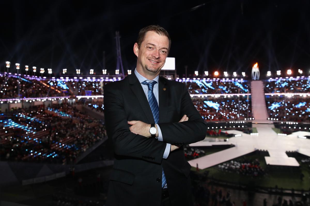 IPC President Andrew Parsons smiles and crosses arms with the PyeongChang 2018 stadium in the background during the Closing Ceremony