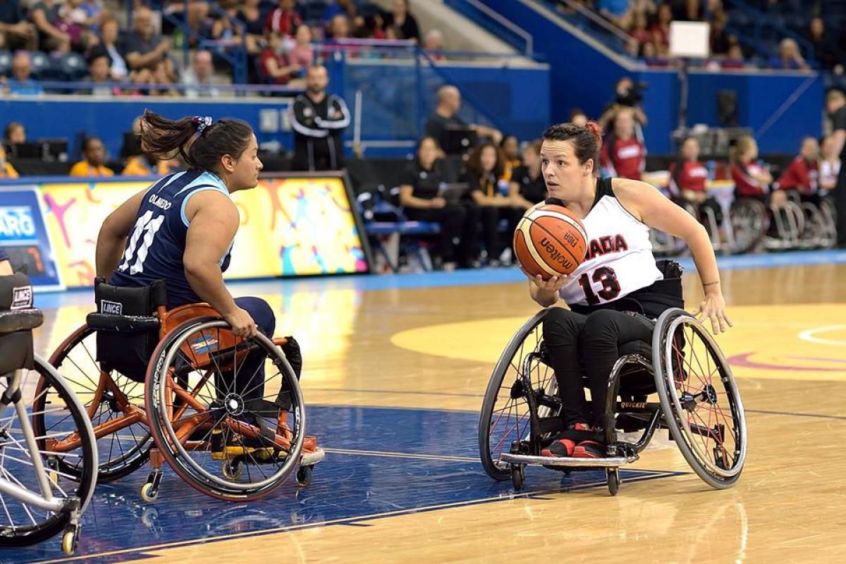 Canadian wheelchair basketball player holds the ball as an Argentinian defender tries to prevent her from scoring