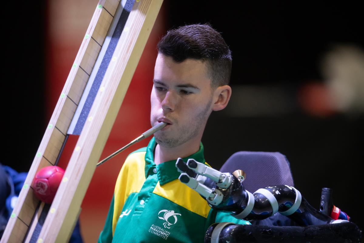 Australian male boccia player holds device in mouth to push ball down ramp