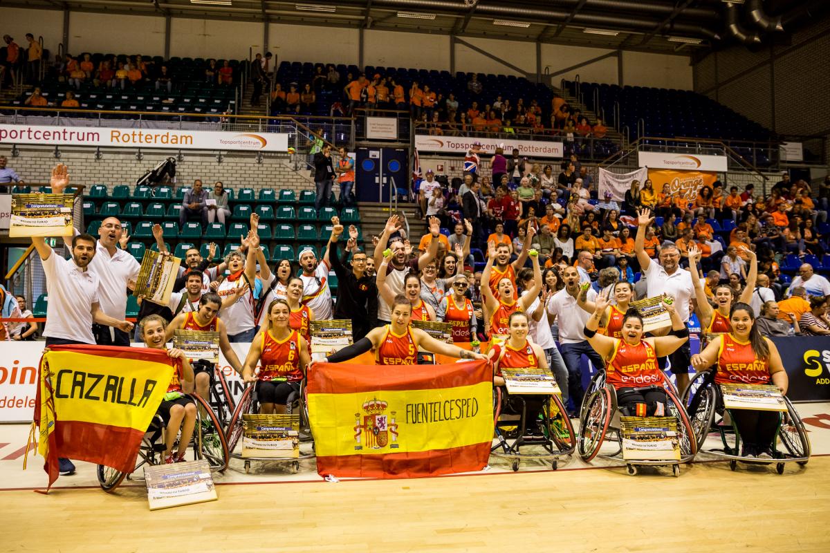 Spanish women's wheelchair basketball team and their staff celebrate as a group holding their hands up