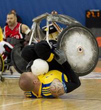 A picture of man in a wheelchair with a ball in his hands falling down.